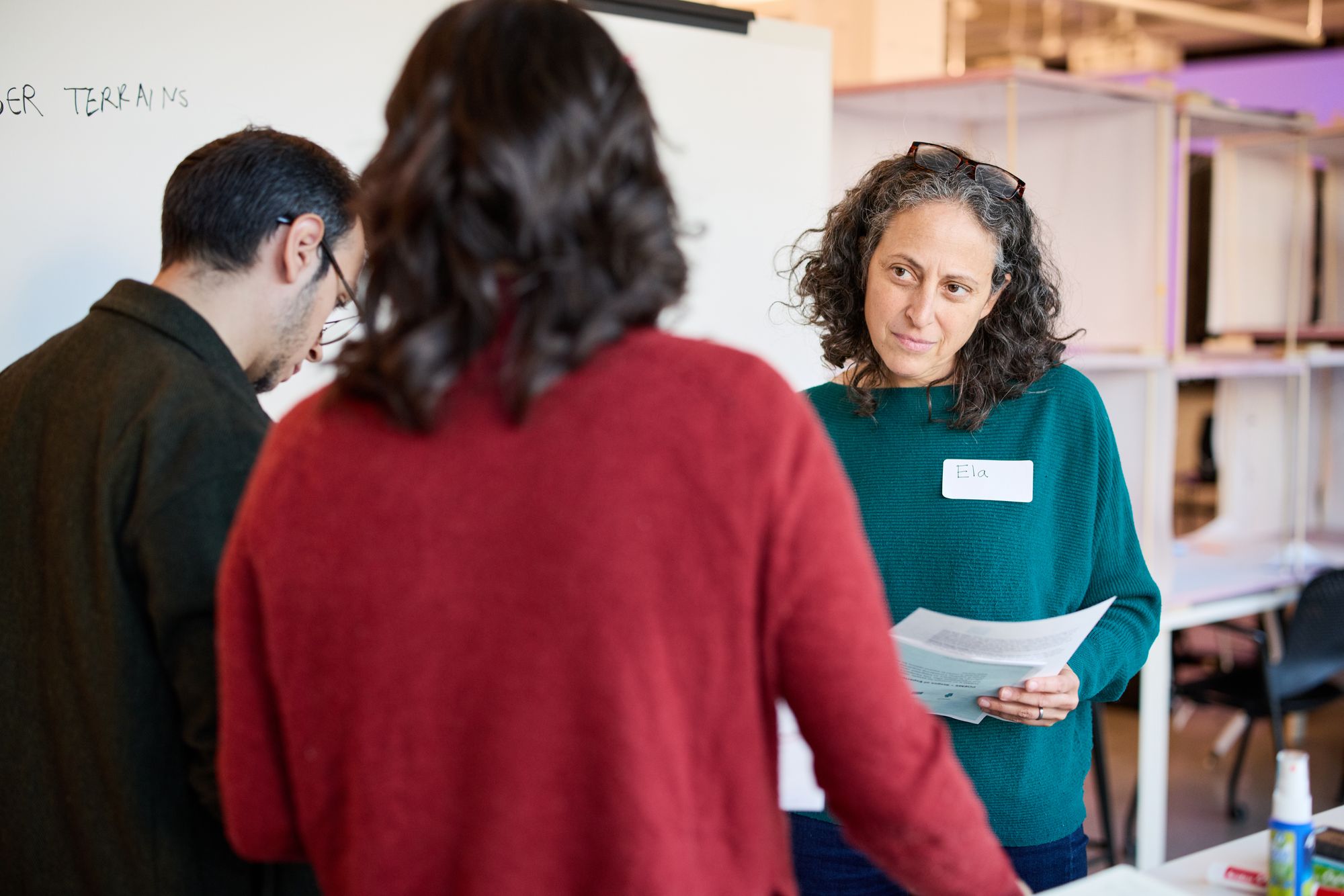 Workshop participants talk, holding their sheets.